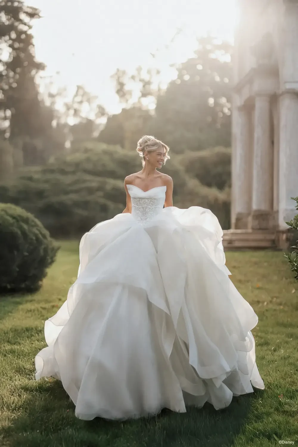 A bride in a flowing white wedding dress stands outdoors, surrounded by greenery.
