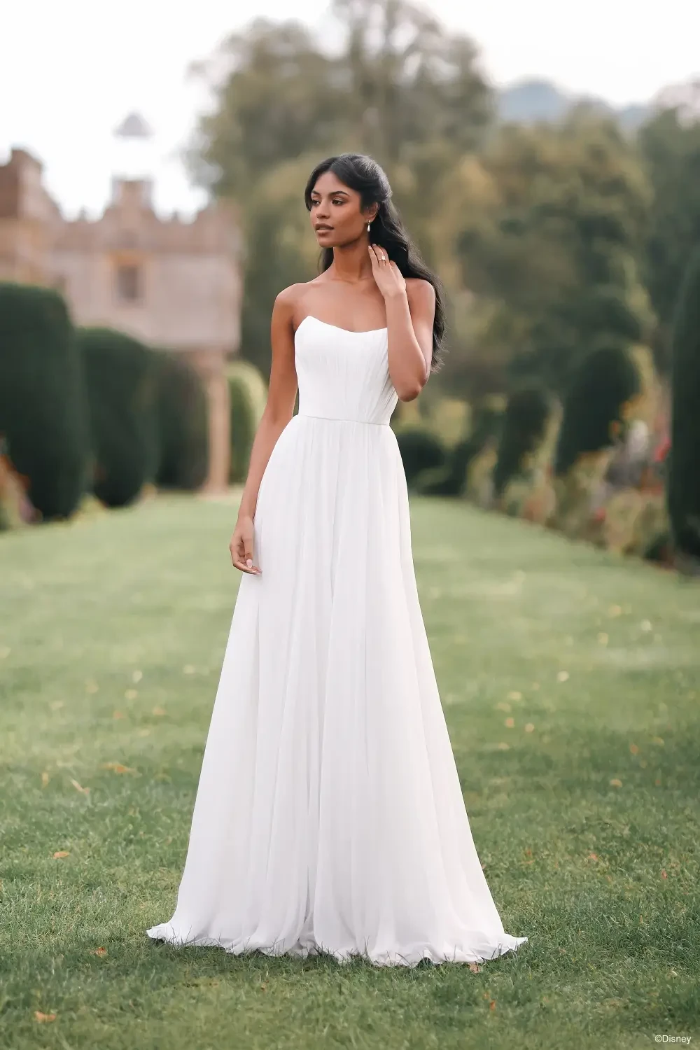 A woman in a white dress standing in a garden with lush greenery.